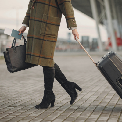 A woman in a plaid coat with a suitcase and handbag walking at the airport